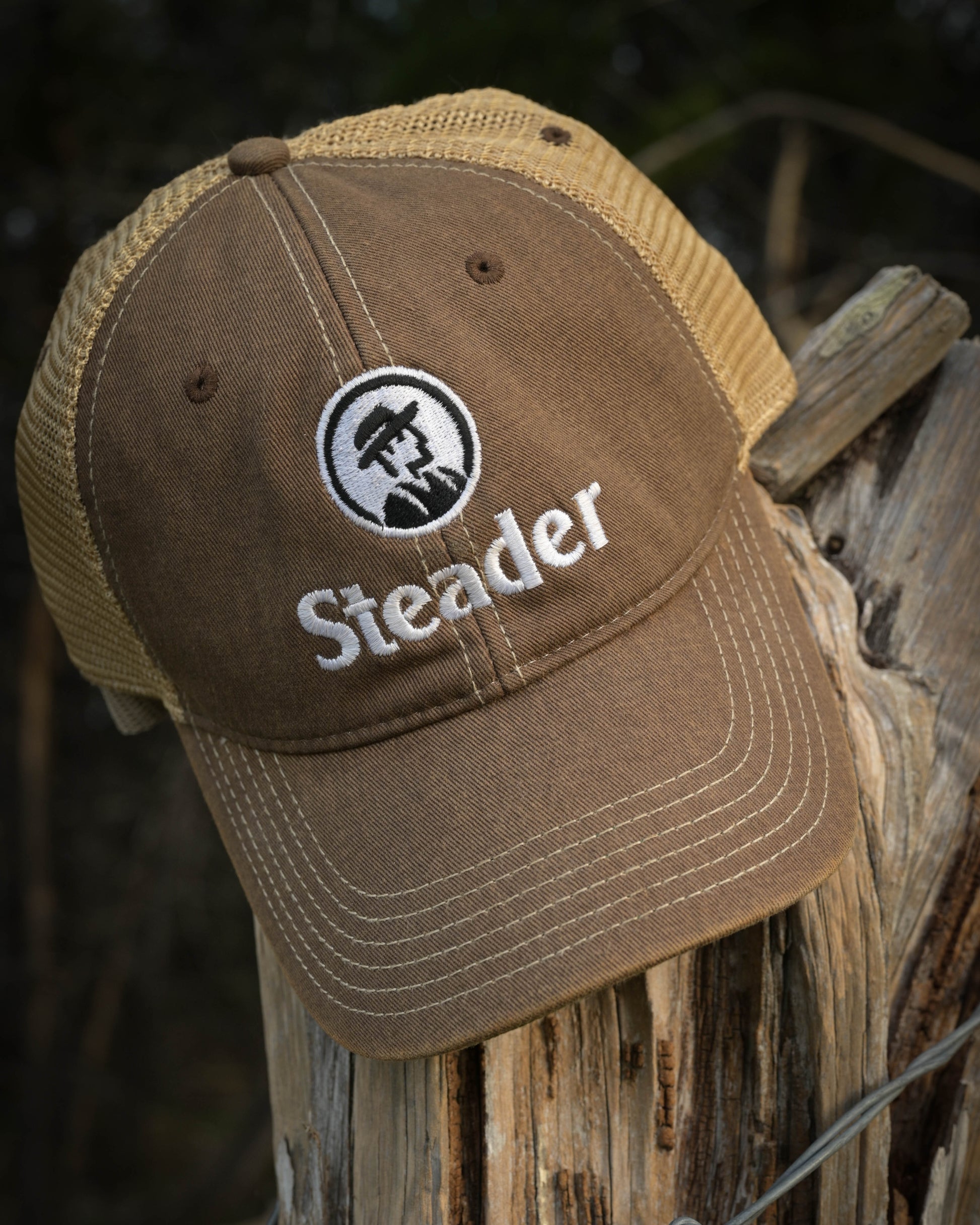 Brown cap with 'Steader' logo on a wooden post