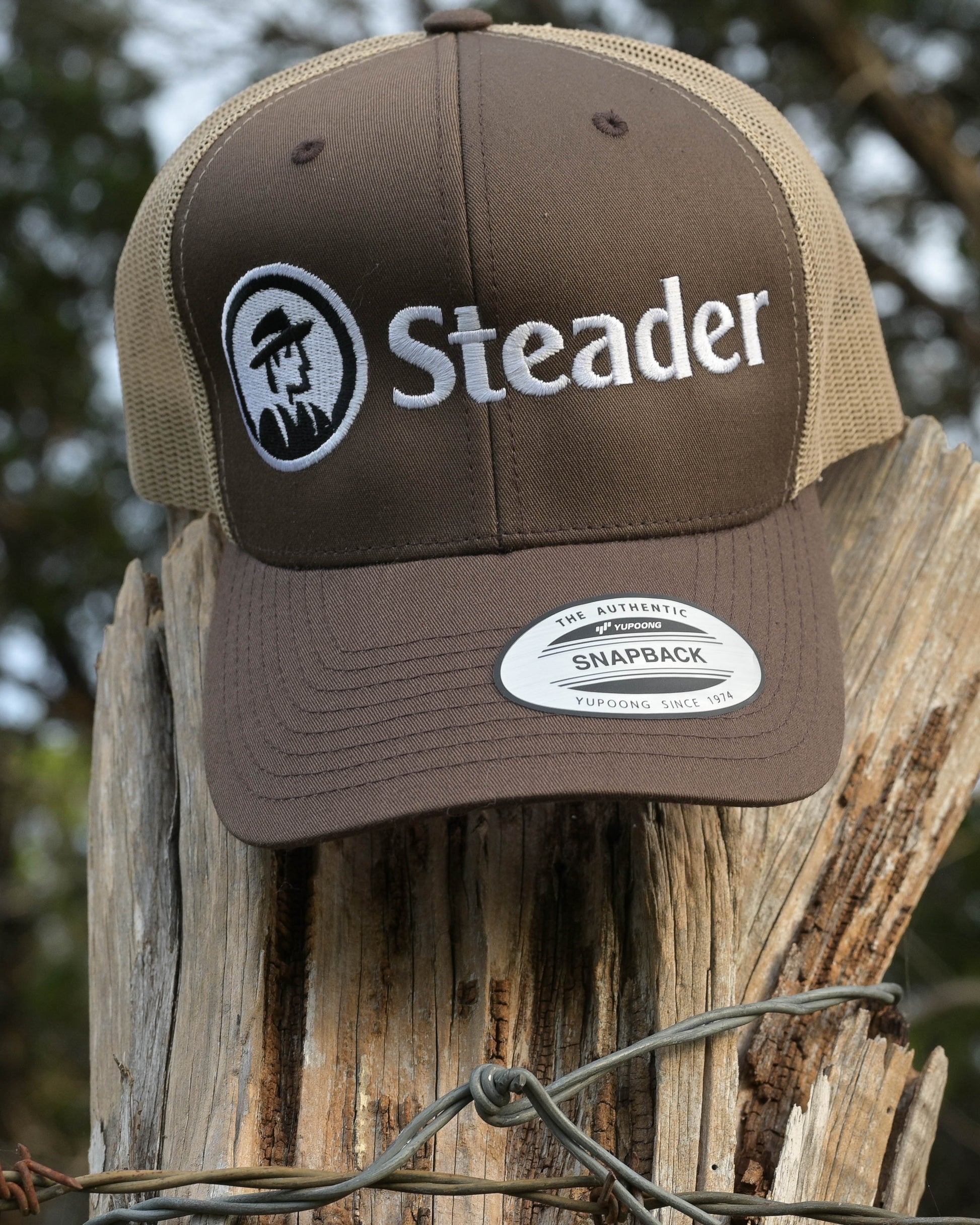 Brown cap with 'Steader' logo on a wooden post with blurred natural background